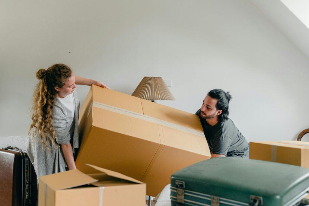 A couple is lifting a huge carton as they are preparing their move